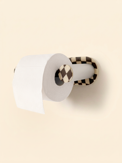 Checkerboard special-edition Roto toilet paper holder mounted on a cream wall with a roll, shown at an angle.